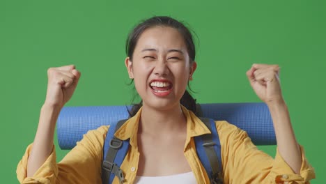 close up of asian female hiker with mountaineering backpack screaming goal celebrating the success while standing on green screen background in the studio