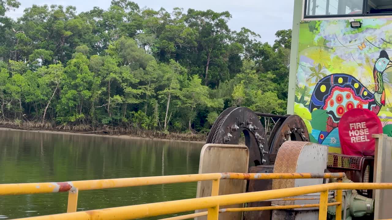 Ferry cable mechanism operates across calm river, lush mangrove rainforest, overcast daylight, steady camera
