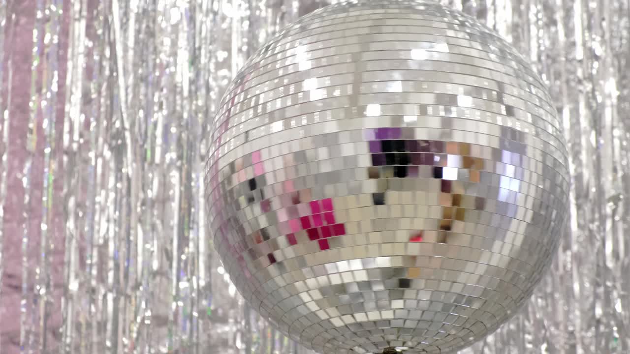 Palla da discoteca rotante su sfondo di una parete decorata con paillettes argentate.