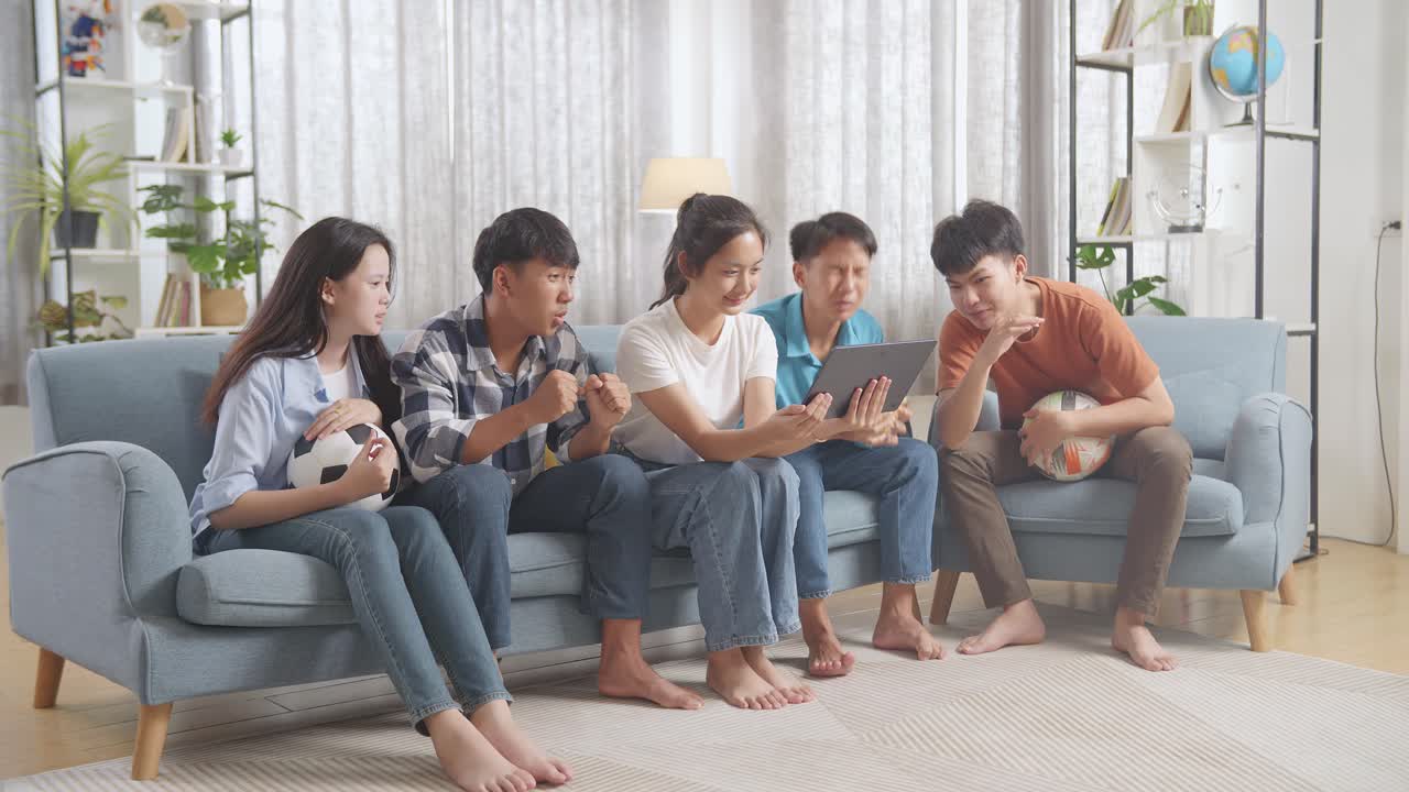 아시아 십대들이 태블릿에서 축구 경기를 응원하고 지켜보고 있습니다. 팀은 승리를 축하하고 팀은 실망합니다.