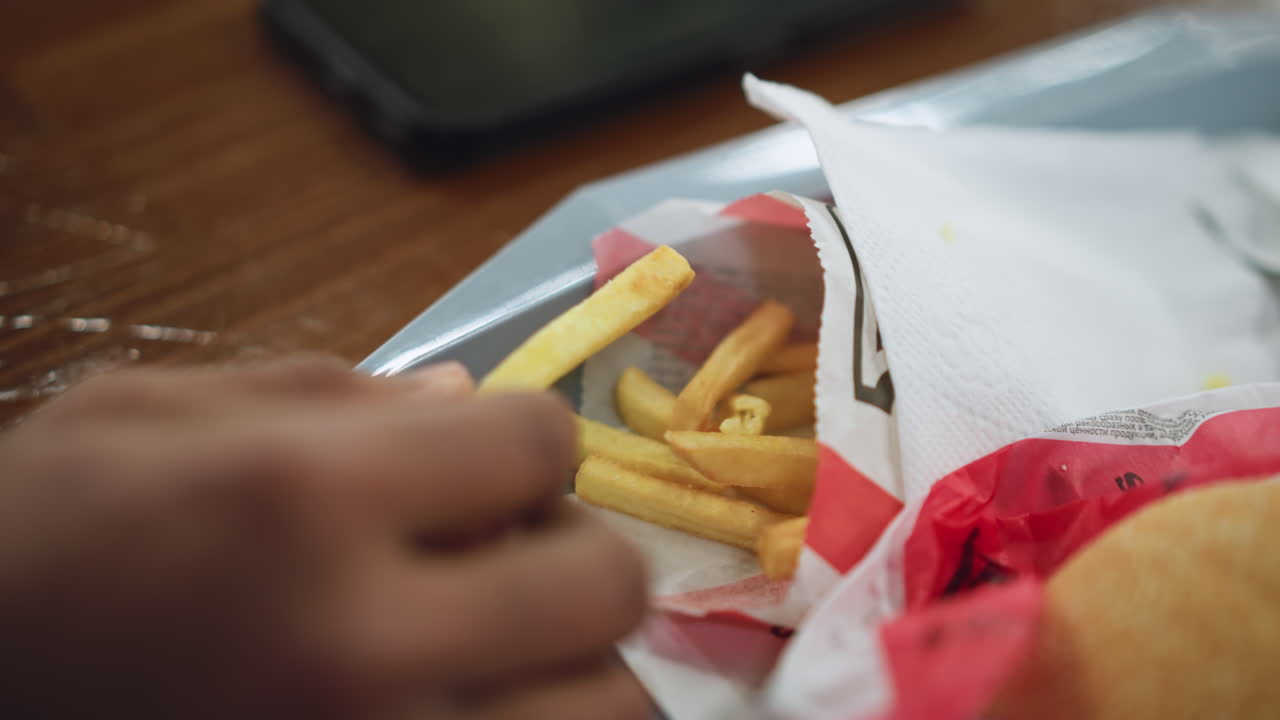 Close view of hand grabbing french chips on tray with crisp texture visible, light reflecting on golden surfaces, shallow depth of field drawing attention to snack, casual eating mood implied