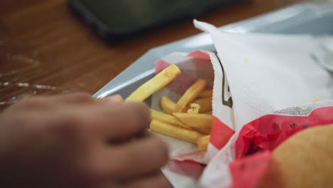 close view of hand grabbing french chips on tray with crisp texture visible, light reflecting on golden surfaces, shallow depth of field drawing attention to snack, casual eating mood implied