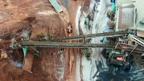 overhead shot of telescopic wheel loader driving underneath conveyor belt system in action at plywood sawmill during waste material management process