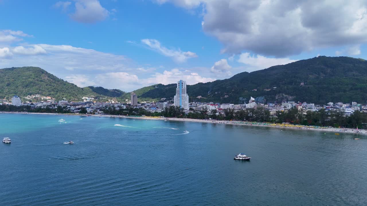Drone footage captures boats and jet skis on the vibrant waters of Patong Beach, Phuket, under a bright blue sky