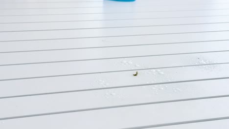 a person wearing pink rubber gloves wipes a white slatted outdoor table with a cloth and cleaning spray in bright, natural daylight