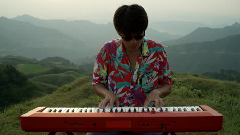 closeup shot asian male musician plays red piano outdoors at natural landscape, wearing vintage clothing, hawaiian shirt and sunglasses