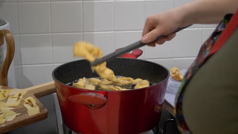 woman taking out cooked angel wings pastry in hot oil