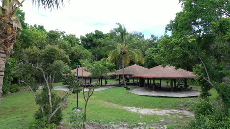 daytime aerial dolly reveal from park gazebo shelters in the green woodland waterfront in miami area