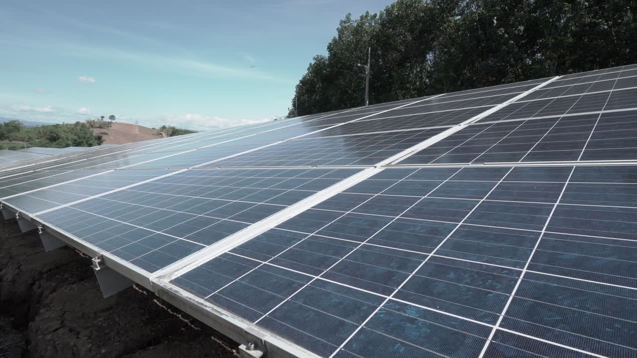 clip de 4k izquierda de paneles solares en una planta de energía solar de energía renovable en las colinas cerca de un bosque