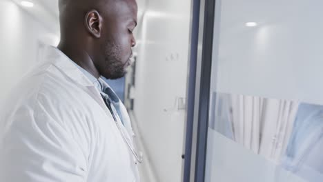 Stressed-african-american-male-doctor-leaning-on-door-in-hospital-in-slow-motion