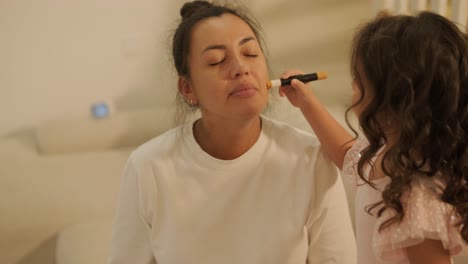 little girl applying makeup to her pregnant mother at home