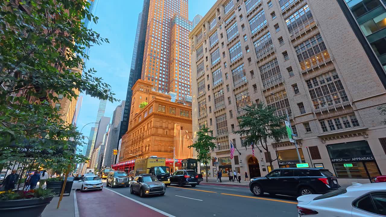 New York, USA, 7 agosto 2025: Vista stradale urbana della Carnegie Hall e dei grattacieli di Manhattan. Ampia prospettiva della 57esima Strada con architettura storica e imponenti edifici moderni in vetro.