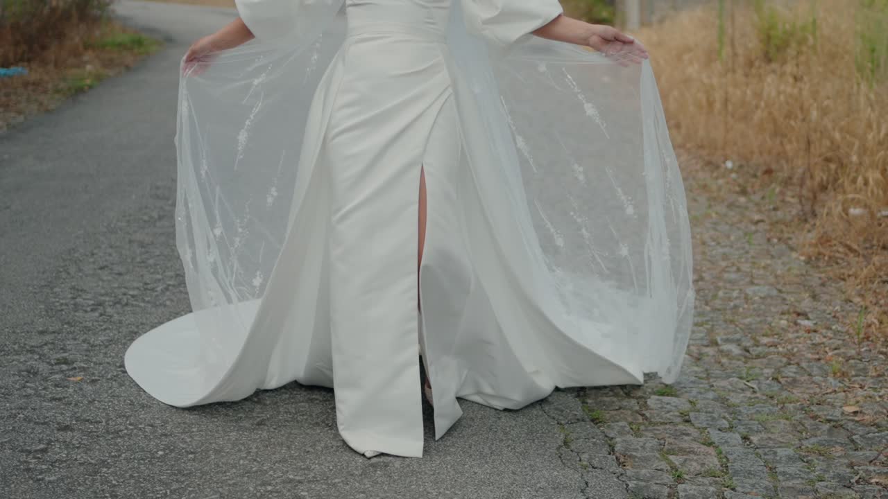 Bride walking on a cobblestone path, holding the flowing fabric of her white gown with a slit
