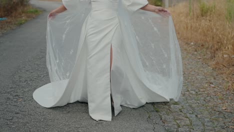 bride walking on a cobblestone path, holding the flowing fabric of her white gown with a slit