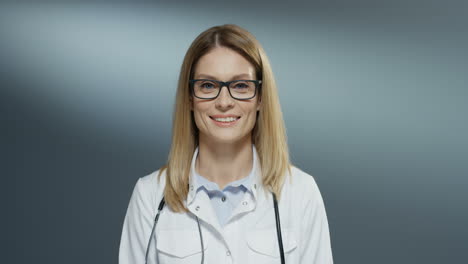 Portrait-Shot-Of-The-Young-Beautiful-Blonde-Woman-Doctor-In-Glasses-And-White-Medical-Gown-Smiling-Happily-To-The-Camera
