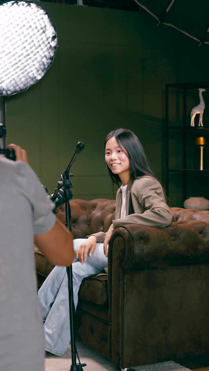 Videografo che riprende una giovane donna seduta in poltrona in studio