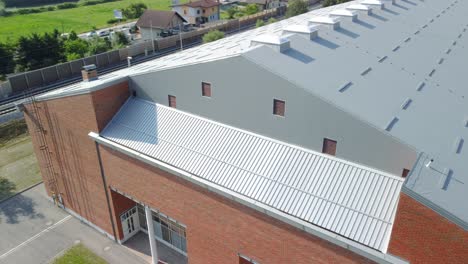 Flying-beside-red-clay-bricks-build-sports-hall-with-grey-insulation-panels-used-for-roof-top