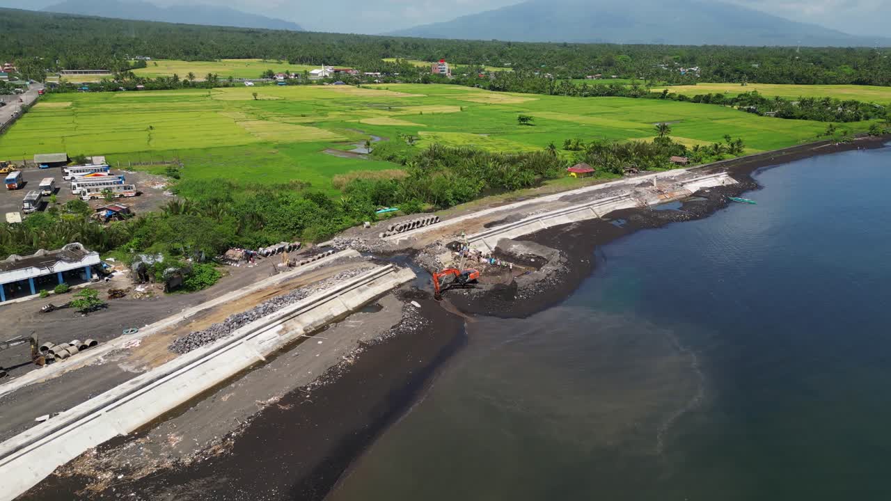 Backhoe Excavator Digging Earth On The Coastal Town Of Malilipot In Albay, Philippines. Aerial Drone Shot