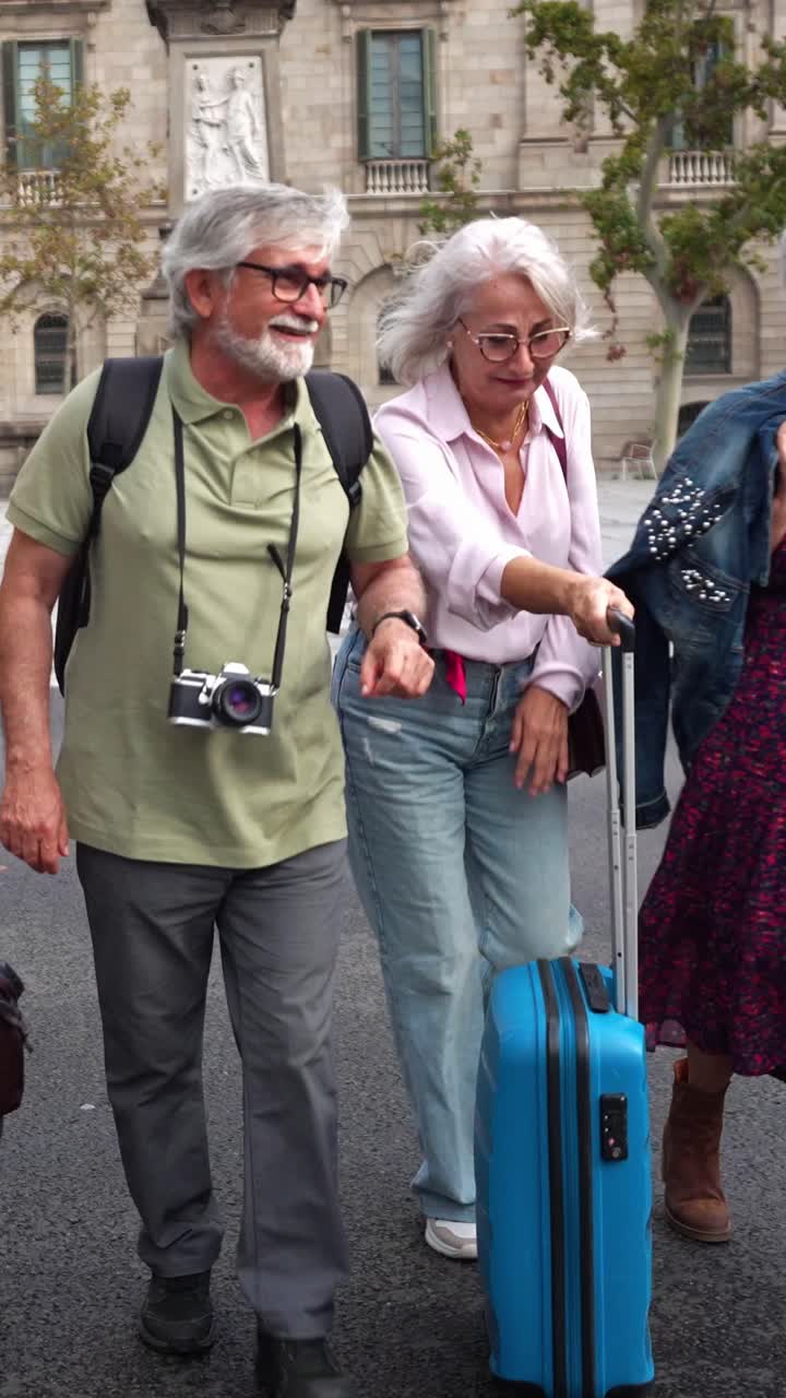 Amici anziani felici che camminano e ridono per una strada cittadina con i bagagli