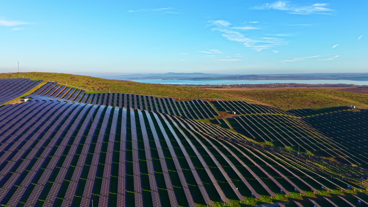 Store solpaneler funkler under den klare, blå himmel på en solskinsdag nær et roligt vandområde, hvilket viser vedvarende energi i et smukt landskab