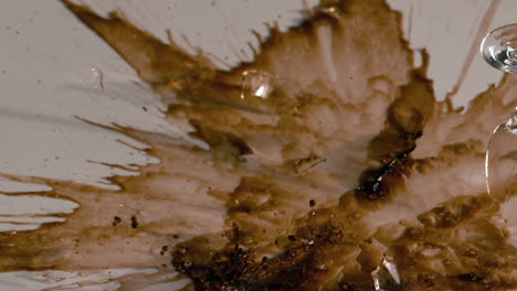 Wine-glass-of-brown-liquid-smashing-onto-white-surface