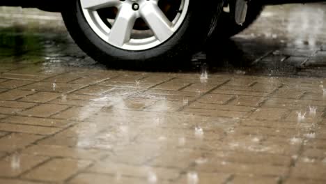 close-up of a car wheel, cars are wetted in parking lot, large drops fall with splashes into puddles, there is heavy rain, downpour, the whole parking lot is flooded with water
