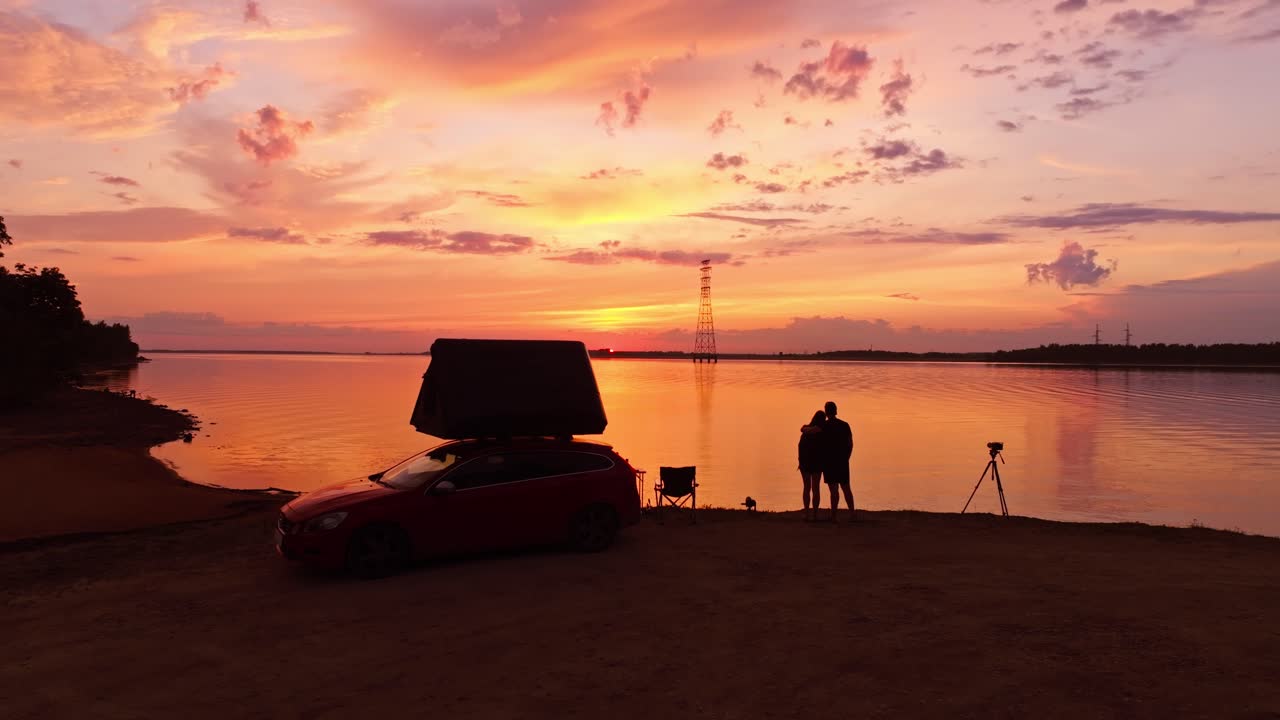 Man embraces woman at Daugmale Latvia while watching Riga hydropower lake sunset
