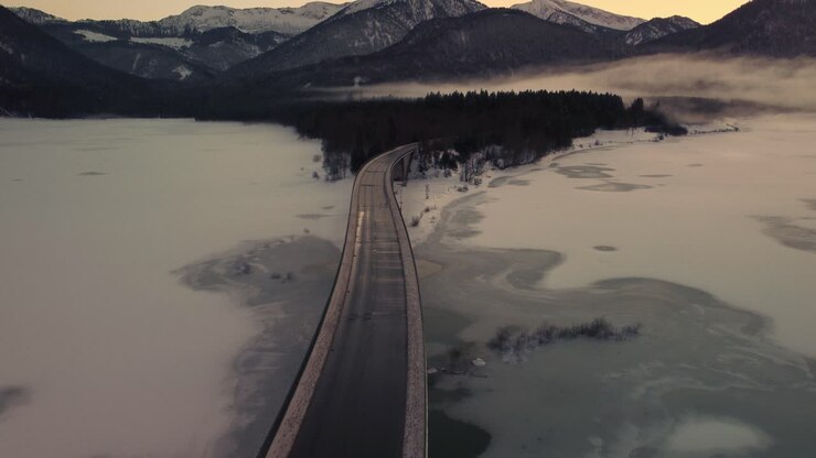Sylvenstein fresh drinking water reservoir bridge in the scenic Bavarian Austrian alps in snow winter with mountains and clear blue water by sunset