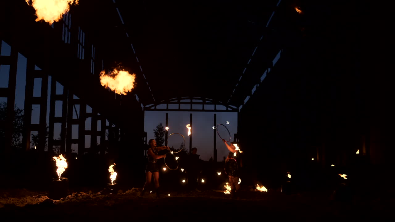 A group of people with fire and torches dancing at sunset in the hangar in slow motion. Fire show.