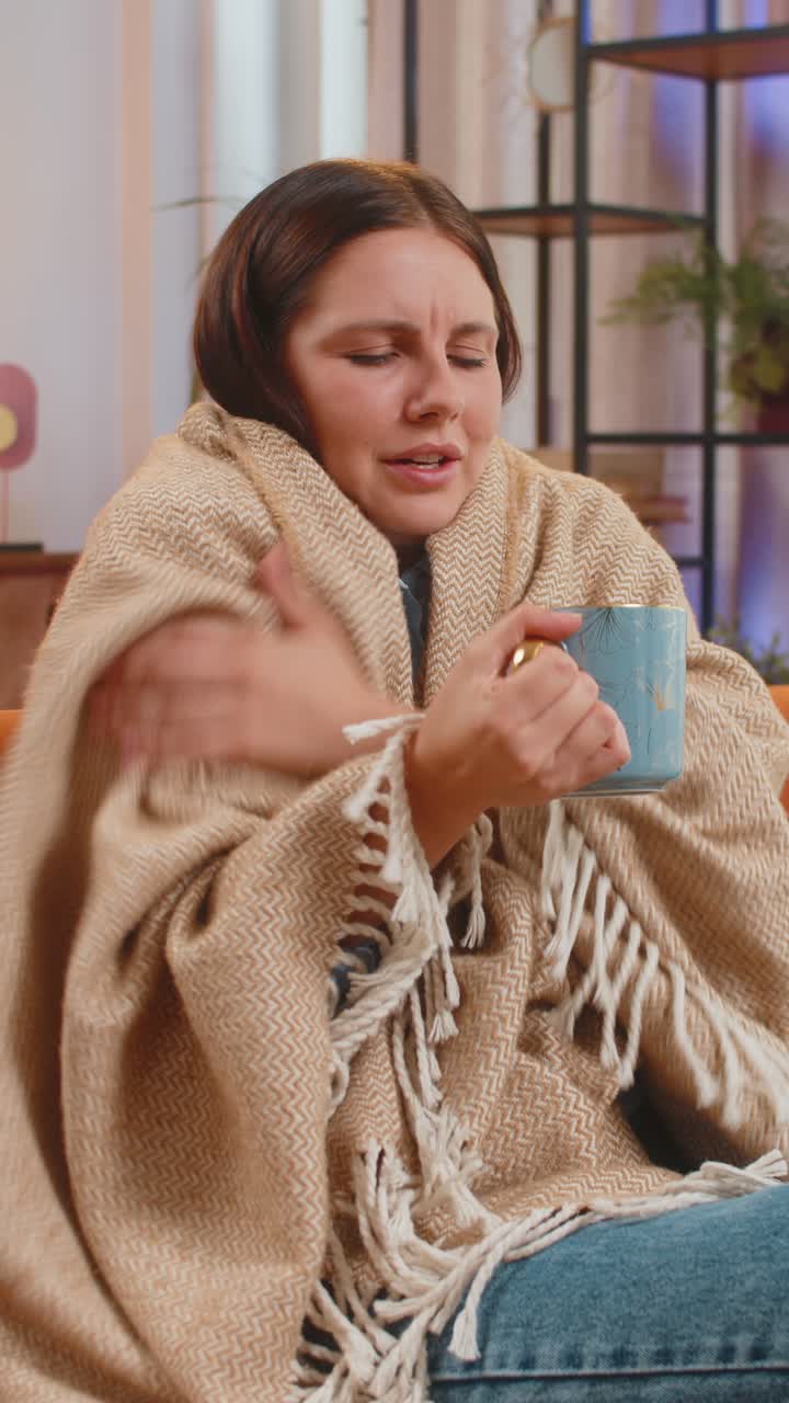 joven enferma enferma cubierta por una manta cálida bebe café se congela de la gripe frío en casa