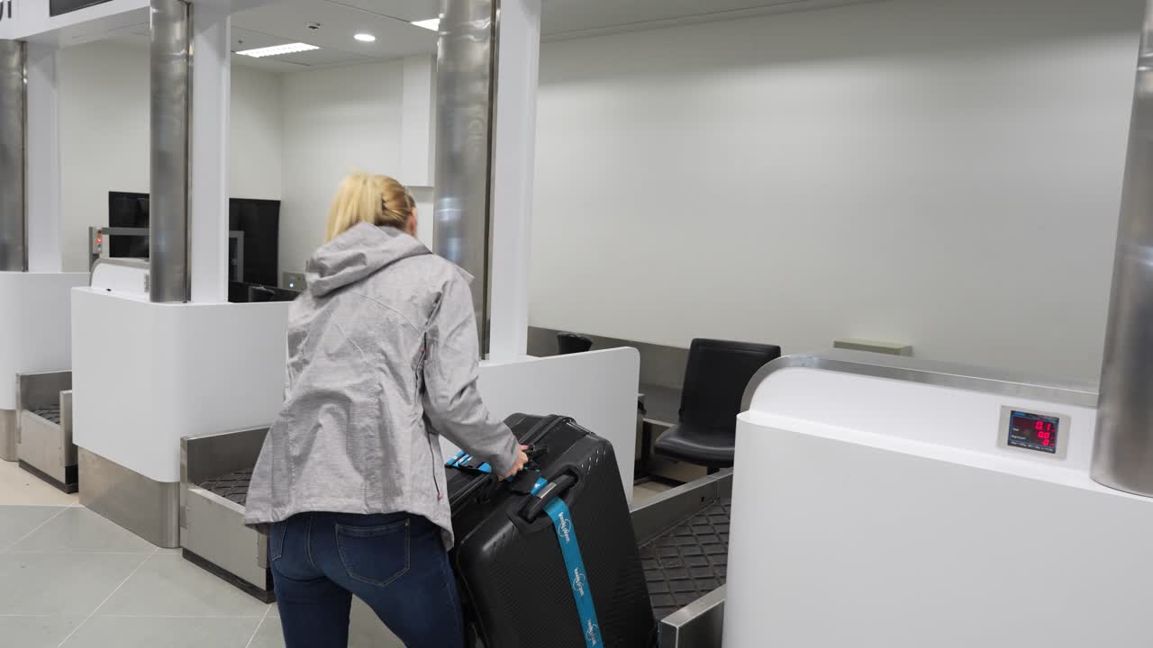 Young woman checking luggage weight at the airport counter