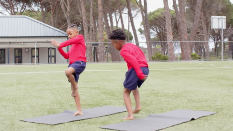 multiracial boys practicing yoga on mats on school field, focusing and balancing in school activity
