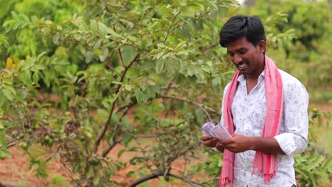 happy young indian farmer counting money at the farm - concept showing of farmer got more profit from the good crop yield