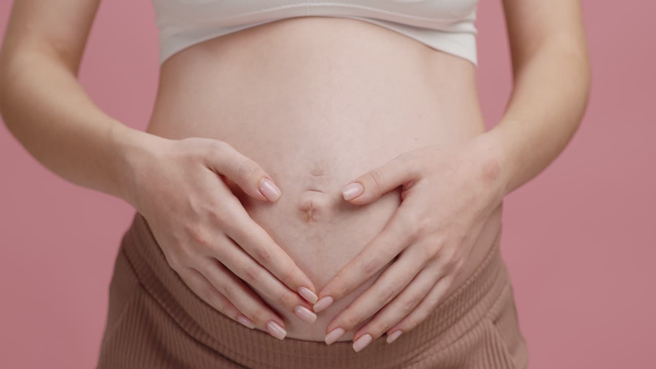Donna incinta con le mani che formano un cuore sulla pancia