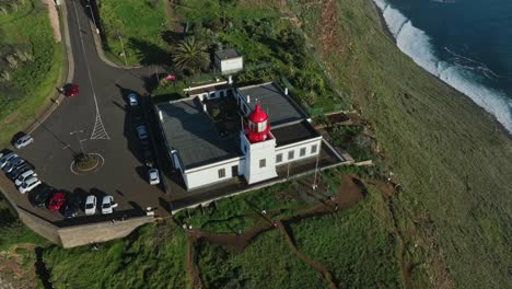 Die-Drohne-Steigt-Mittags-Auf-Und-Neigt-Sich-Zum-Rot-weißen-Leuchtturm,-Der-Auf-Einer-Steilen-Felsklippe-Errichtet-Wird