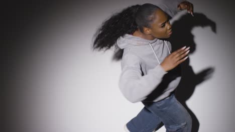 looking down on studio shot of young woman dancer wearing hoodie dancing in spotlight in slow motion