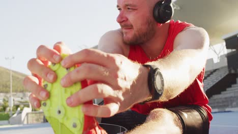 caucasian disabled male athlete with running blade wearing headphones and stretching