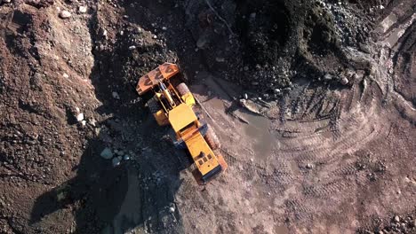 Large-powerful-yellow-placer-mining-wheel-operating-yellow-loader-in-Yukon-brown-dirt-ground,-Canada,-directly-above-aerial