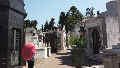 single tourist with sun umbrella walk inside recoleta cemetery mausoleums
