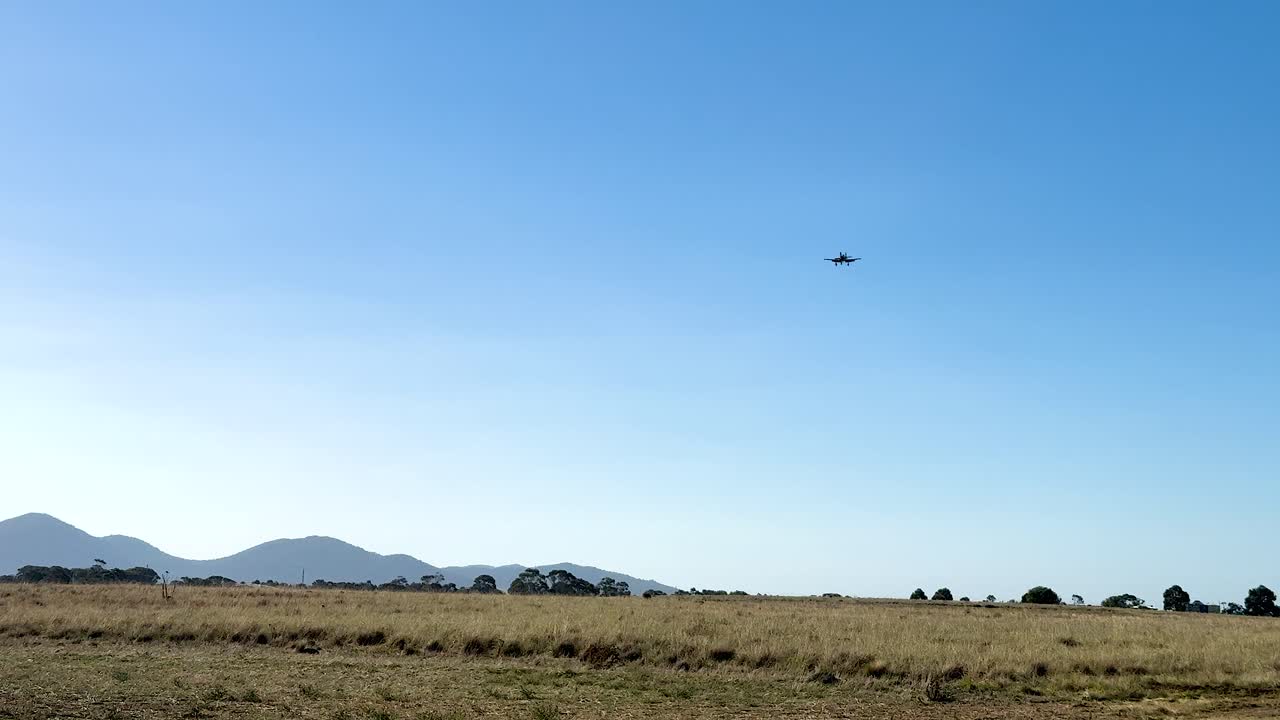 A Hawker Sea Fury aircraft flies across a clear blue sky over Geelong, captured in bright daylight with distant mountains