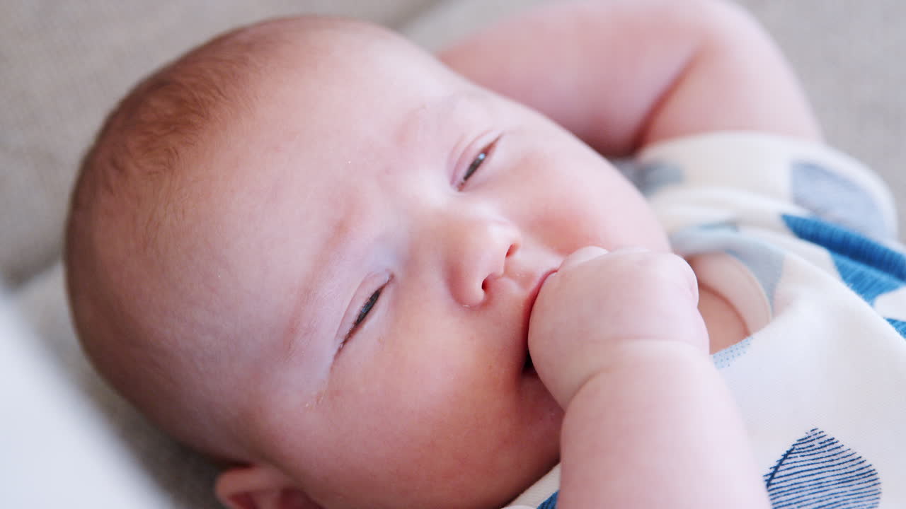 새로 태어난 아기 소년 이 집 에서 소파 에 손 을 넣고 누워 있는 느린 움직임 의 클로즈업  ⁇