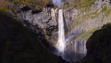 breathtaking waterfall falling in between high rocks with rainbow forming