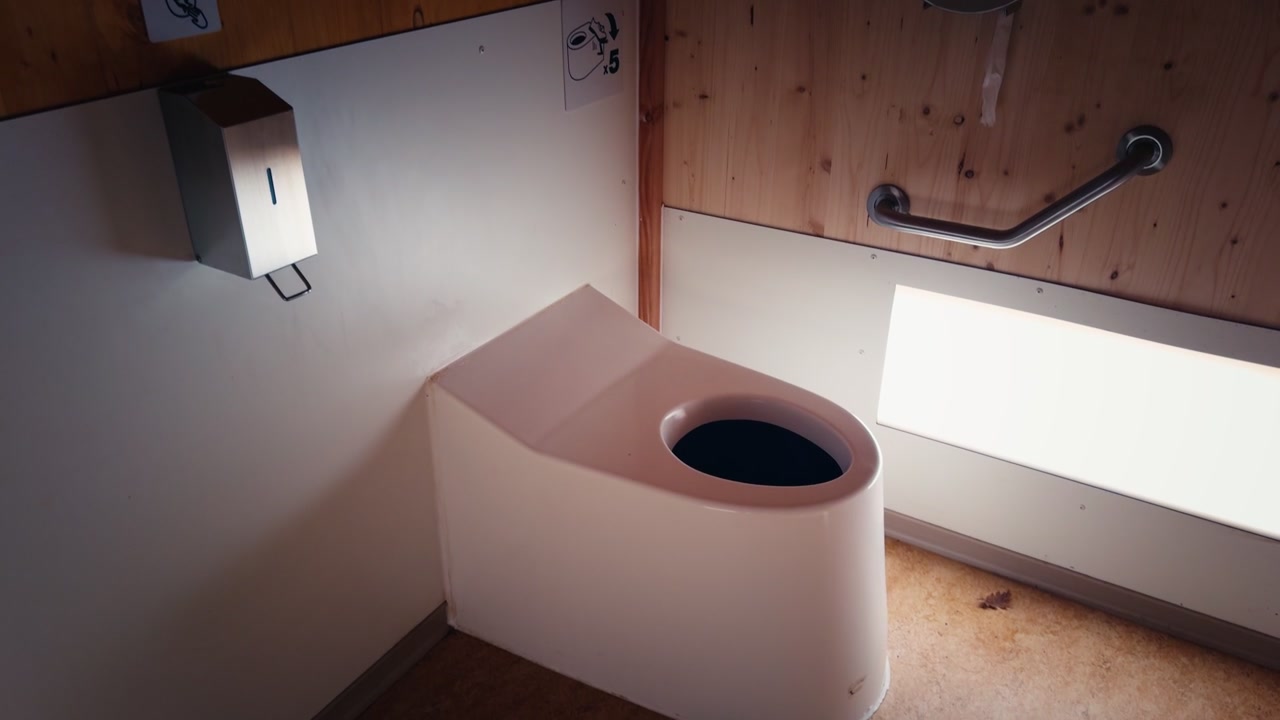 Clean and minimalist white composting toilet seat positioned in a wooden paneled restroom. A modern ecological solution for waste management and water scarcity.