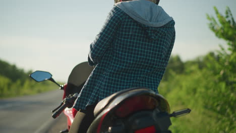 a female biker wearing a helmet climbs onto her motorcycle, preparing to ride, the background is blurred with lush greenery