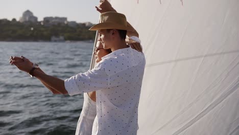 sailing boat - romantic young couple enjoying time together on small cruise ship sailing on open sea. woman and man in love on boat travel sailing during vacation, guy holding a hand of his girlfriend pointing on horizon