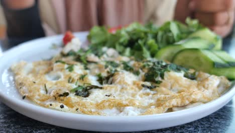 a plate of scrambled eggs with a side of salad and cucumber