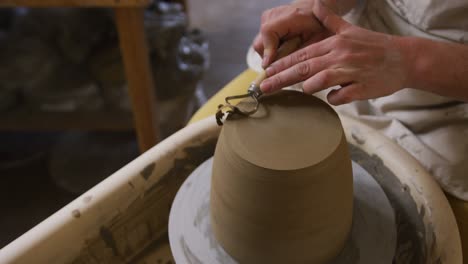 close up view of female potter using loop tool for finishing pottery at pottery studio