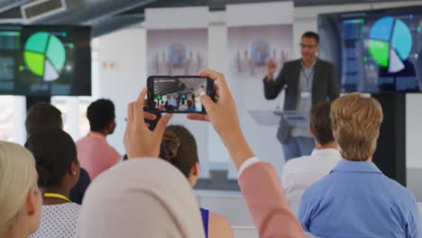 woman in audience at a business conference filming with smartphone