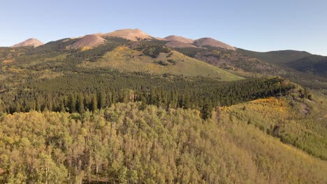 Aerial-dolly-view-overflying-a-remove-ridge-covered-in-aspen-towards-a-distant-series-of-rocky-peaks