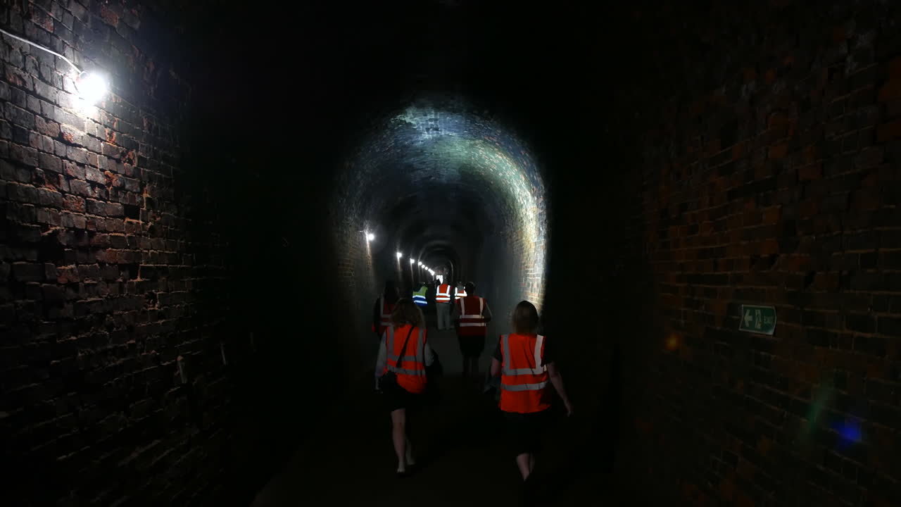 Group of People Walking Through a Dark Brick Tunnel